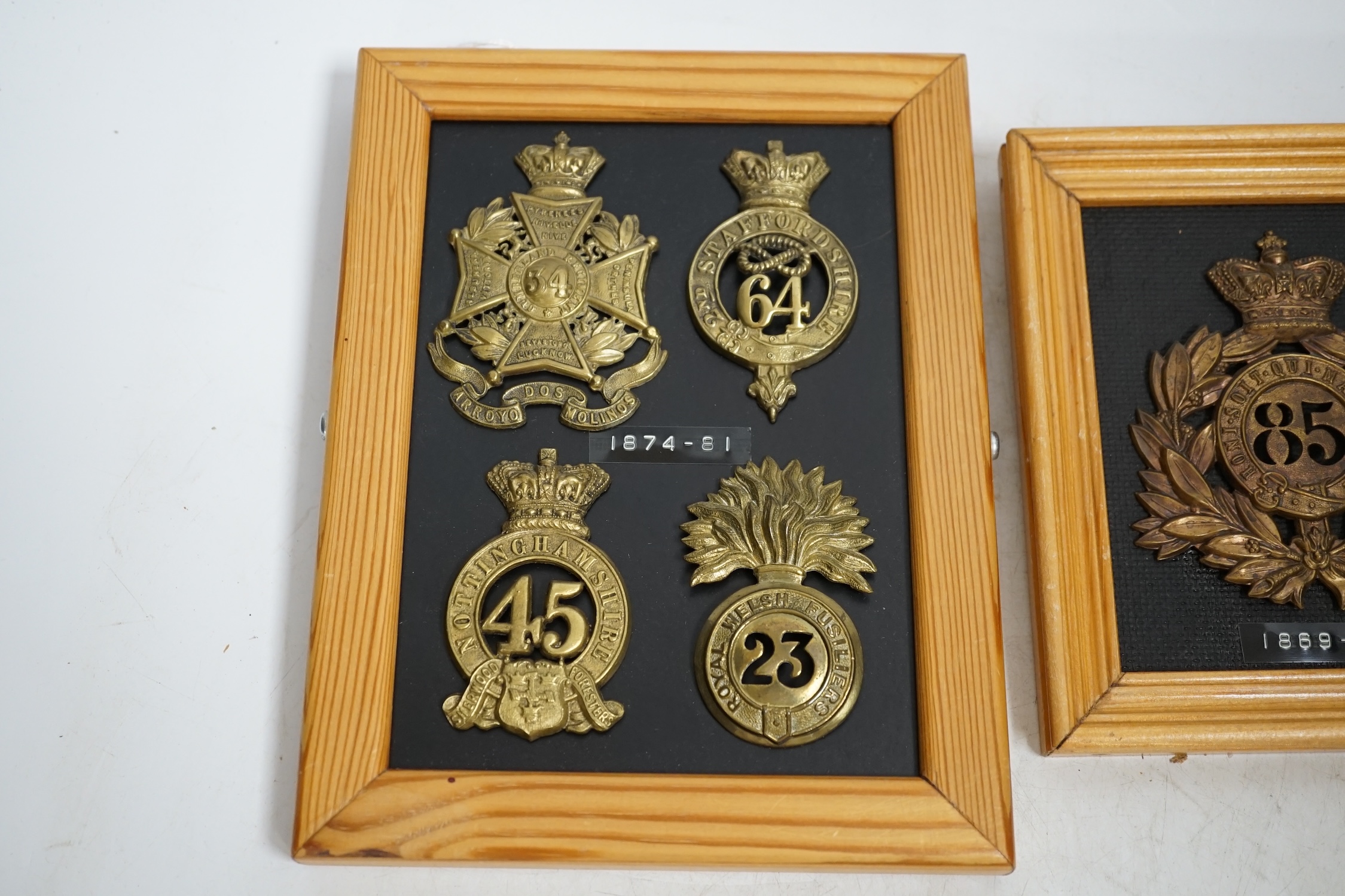 Five military helmet and shako plates mounted on two boards, including; the Nottinghamshire Regiment, the 2nd Staffordshire Regiment, the Royal Welsh Fusiliers, the Cumberland Regiment and the 85th King’s Light Infantry.